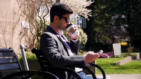 Man-using-mobile-phone-while-having-coffee-in-park-4k