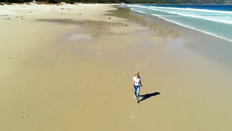 Aerial-of-woman-walking-on-beautiful-beach-4k