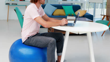 Männliche-Führungskraft-Benutzt-Laptop,-Während-Sie-Auf-Dem-Gymnastikball-Am-Schreibtisch-Sitzt-4k