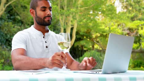Hombre-Sonriente-Usando-Laptop-Mientras-Toma-Vino-En-El-Jardín-4k