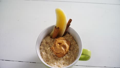 Cup-of-oats-with-peanut-butter,-banana-and-cinnamon-sticks-4k