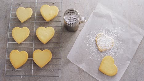 Raw-heart-shape-cookies-on-baking-tray-with-flour-shaker-strainer-and-wax-paper-4k