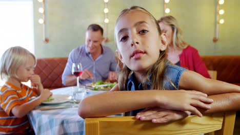 Smiling-girl-looking-at-camera-while-family-having-food-in-background-4k