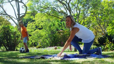 Mother-spreading-the-picnic-blanket-and-son-playing-football-in-park-4k