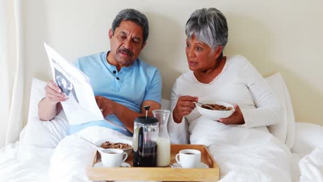 Senior-couple-reading-newspaper-while-having-breakfast-in-bedroom-4k