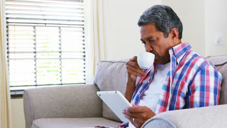 Älterer-Mann-Nutzt-Digitales-Tablet-Beim-Kaffeetrinken-Im-Wohnzimmer-4K