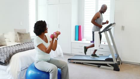 Woman-exercising-with-dumbbells-while-man-jogging-on-treadmill-4k