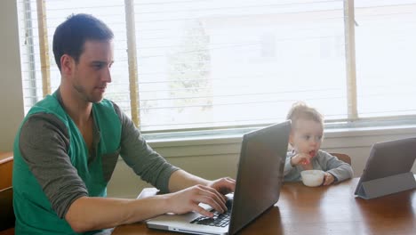 Father-using-laptop-while-baby-boy-having-breakfast-4k