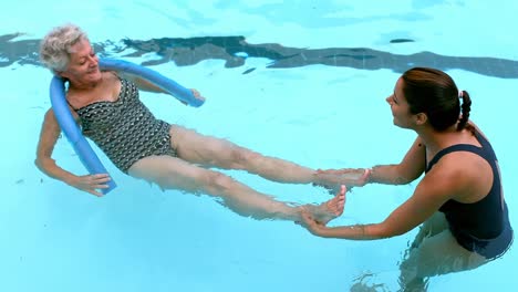Female-coach-helping-senior-woman-in-swimming-pool