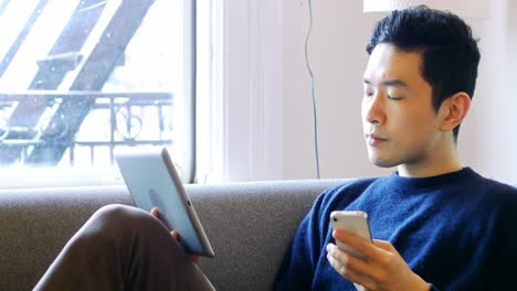 Hombre-Usando-Tableta-Digital-Y-Teléfono-Móvil-En-La-Sala-De-Estar-4k