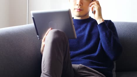 Man-talking-on-mobile-phone-while-using-digital-tablet-in-living-room-4k