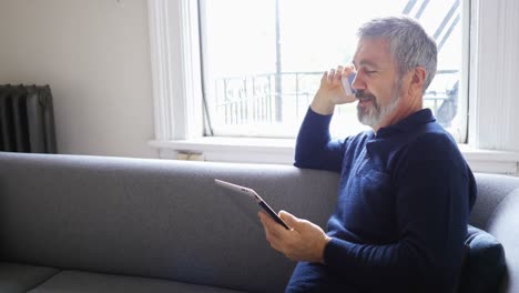 Man-talking-on-mobile-phone-while-using-digital-tablet-in-living-room-4k