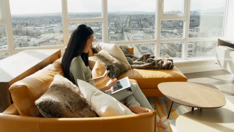Woman-using-digital-tablet-while-having-coffee-in-living-room-4k