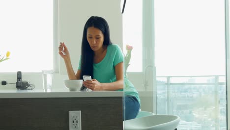 Mujer-Usando-Teléfono-Móvil-Mientras-Desayuna-En-La-Cocina-4k