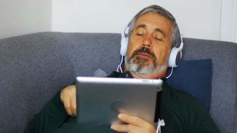 Mann-Hört-Musik-Auf-Einem-Digitalen-Tablet,-Während-Er-Auf-Dem-Sofa-Liegt-4k