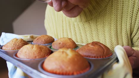 Senior-woman-smelling-freshly-baked-muffins-in-the-tray-4K-4k