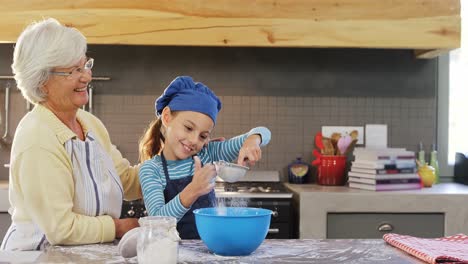 Little-girl-with-chef-cap-sieving-flour-and-looking-at-grandma-4K-4k