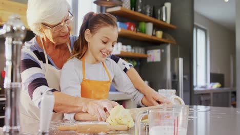 Grandmother-and-little-girl-in-apron-flattening-dough-with-rolling-pin-4K-4k