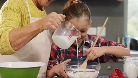 Girl-mixing-the-flour-while-grandmother-pouring-milk-into-the-bowl-4K-4k