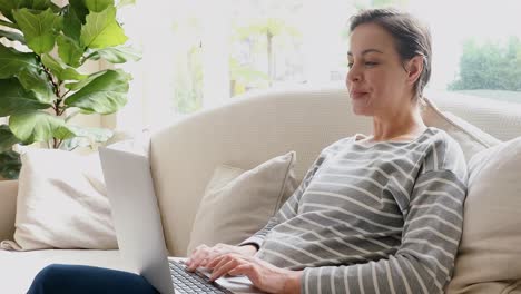 Happy-young-woman-sitting-on-sofa-having-a-video-call-on-her-laptop-4K-4k