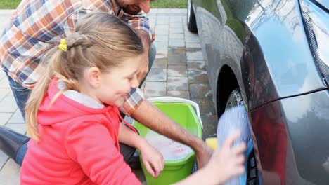 Happy-daughter-and-father-washing-car-tier-with-sponge-4K-4k