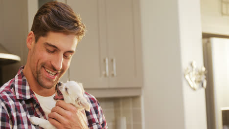 Smiling-young-man-holding-pet-in-his-arms-in-the-kitchen-4K-4k