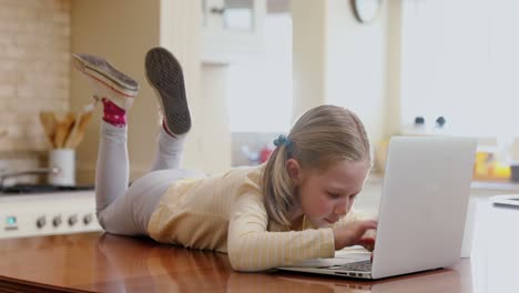 Happy-little-girl-lying-on-table-using-her-laptop-4K-4k