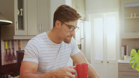 Young-man-wearing-spectacles-sitting-on-stool-having-coffee-while-using-laptop-4K-4k