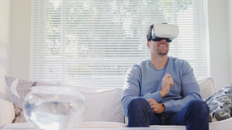 Young-man-sitting-on-sofa-experiencing-virtual-reality-headset-4K-4k