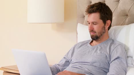 Young-man-sitting-on-bed-using-his-laptop-in-the-bedroom-at-home-4K-4k