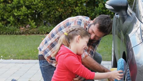 Happy-father-tickling-his-daughter-while-washing-car-tier-with-sponge-4K-4k