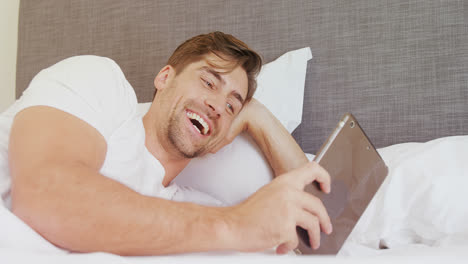 Smiling-man-lying-on-bed-using-his-digital-tablet-4K-4k