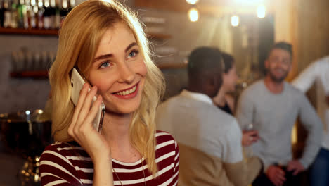 Young-smiling-woman-talking-on-phone-while-friends-interacting-in-background-4K-4k