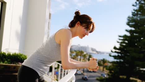 Young-woman-leaning-on-balcony-railing-and-having-coffee-at-home-4k