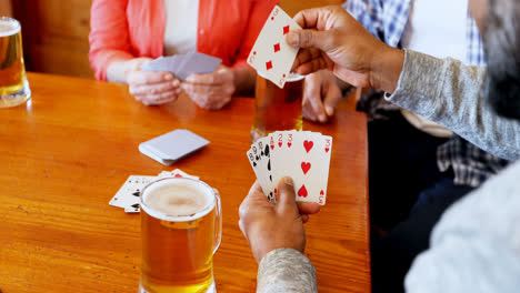 Mid-section-of-friends-playing-cards-while-having-glass-of-beer-4k