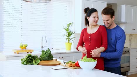 Mann-Umarmt-Schwangere-Frau,-Während-Er-An-Der-Küchentheke-Salat-Zubereitet-4k