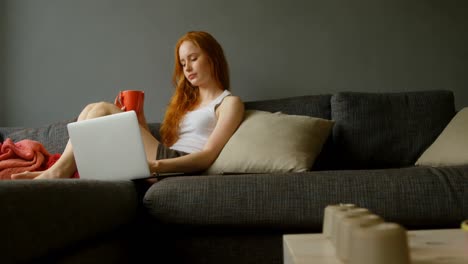 Woman-having-coffee-while-using-laptop-in-living-room-4k