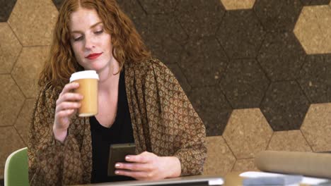 Mujer-De-Negocios-Tomando-Café-Mientras-Usa-El-Teléfono-Móvil-En-La-Oficina-4k