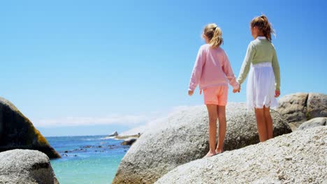 Siblings-holding-hands-with-arms-outstretched-on-a-rock-4k