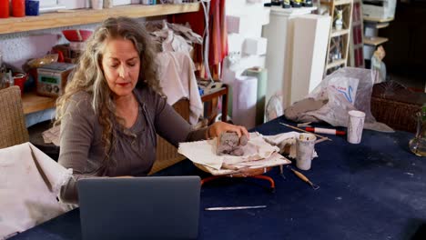 Mature-female-potter-molding-a-clay-while-using-laptop-4k