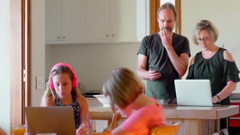 Parents-using-laptop-and-mobile-phone-while-kids-studying-in-kitchen-4k
