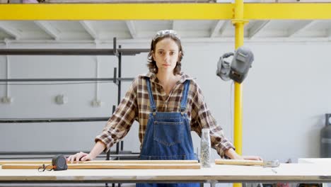 Female-welder-standing-with-wooden-plank-in-workshop-4k