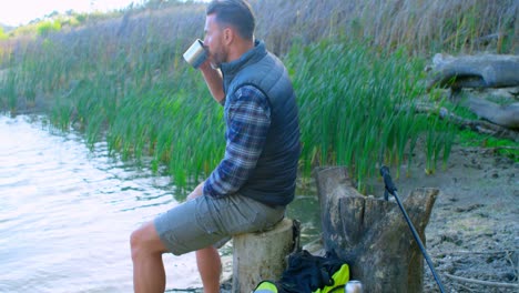 Male-hiker-having-coffee-near-a-lake-4k