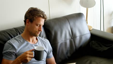 Mann-Trinkt-Kaffee,-Während-Er-Im-Wohnzimmer-Ein-Buch-Liest-4k