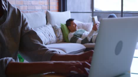 Woman-using-laptop-while-man-reading-book-on-sofa-4k
