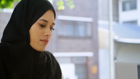 Mujer-Con-Hijab-Trabajando-En-Una-Computadora-Portátil-En-Un-Café-Al-Aire-Libre-4k