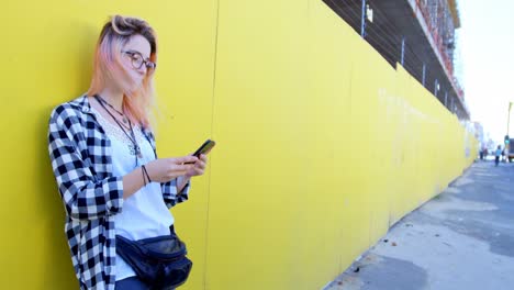 Fashionable-woman-using-mobile-phone-against-a-yellow-wall-4k