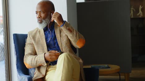 Senior-businessman-listening-to-music-on-headphones-in-office-4K-4k