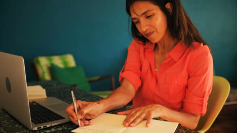 Mujer-Escribiendo-En-Un-Cuaderno-Mientras-Usa-Una-Computadora-Portátil-4k