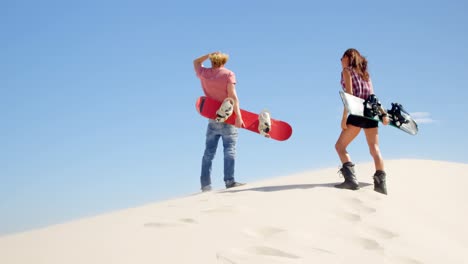 Couple-with-sand-boards-looking-at-a-distance-in-the-desert-4k